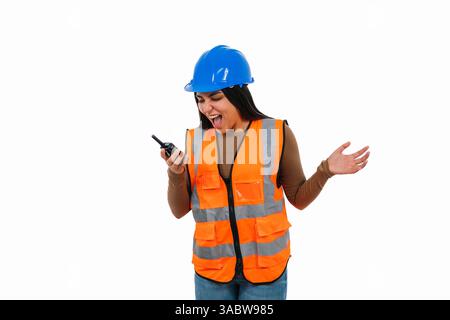 Young female engineer wearing safety helmet and vest communicating with her team using a walkie talkie, shouting and gesturing on white background Stock Photo