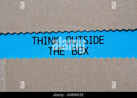 Think outside the box message written on ripped torn paper on blue background. Conceptual think outside the box symbol. Copy space. Stock Photo