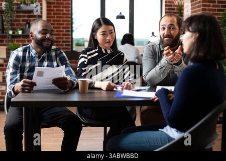 Friendly multiracial HR managers interviewing female candidate at a table, asking about her experience. Diverse recruitment team discussing with potential job applicant. Hiring concept. Stock Photo