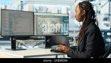 Programmer in photovoltaics factory using PC program to diagnose malfunctioning systems. Woman coding at computer desk in solar panels manufacturing plant, reducing downtime, camera B Stock Photo