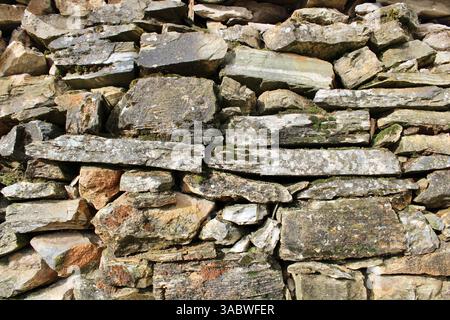 Rustic dry stone wall with flat, horizontal stones and moss. Natural background or texture for rural architecture and building material themes. Stock Photo