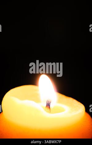 Close up of a flame on a yellow beeswax candle, black background, copy space above Stock Photo