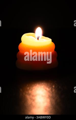Burning beeswax candle shaped like a skep on black background Stock Photo