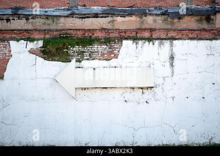 Large metal arrow on cracked and crumbling wall Stock Photo