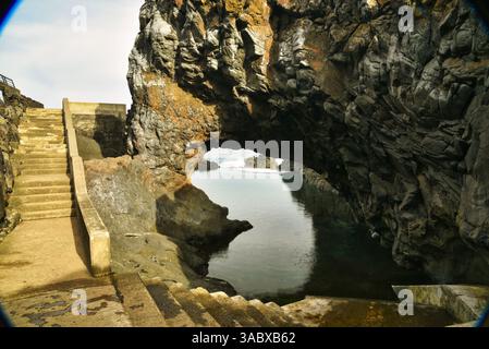 Steps leading down to Poças das Lesmas, a coastal natural swimming pool within arching lava rock outcroppings in Seixal, Madeira Island, Portugal Stock Photo