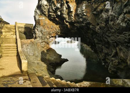 Steps leading down to Poças das Lesmas, a coastal natural swimming pool within arching lava rock outcroppings in Seixal, Madeira Island, Portugal Stock Photo