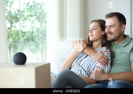 Couple relaxing sitting on a sofa at home with smart speaker Stock Photo