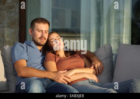 Couple sleeping sitting at sunset in a sofa in terrace at home or hotel Stock Photo