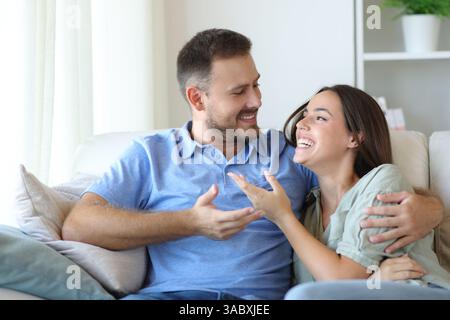 Happy couple in love sitting on a couch talking looking each other at home Stock Photo