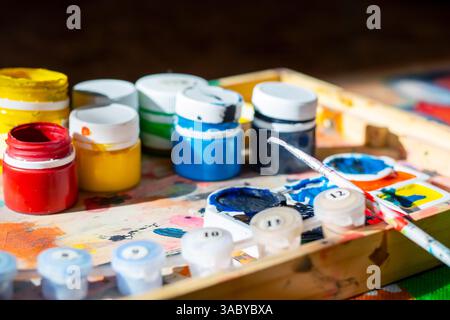 A beautifully crafted wooden tray that is generously filled with an assortment of vibrant bottles of paint and various art brushes Stock Photo