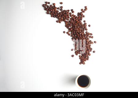 A steaming cup of coffee beside scattered roasted beans on a white background, capturing a fresh, energizing, and minimalist vibe Stock Photo
