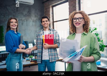 Three young professionals collaborate in a modern office environment, showcasing teamwork, diversity, and a friendly workspace atmosphere. Stock Photo