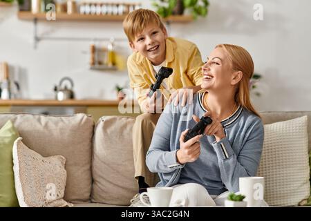 A playful mother and her son enjoy quality time playing video games in their modern living room. Stock Photo