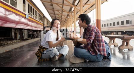 Travel and Companionship. A couple discussing their travel plans while sitting at a train station. Stock Photo