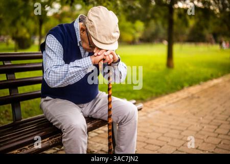 Elderly man sits alone on a wooden bench in the park. He is depressed. Stock Photo