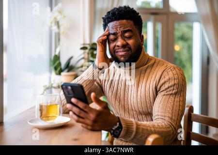 Young black man sitting in bar. He is freelancer on job pause, tired and exhausted. Stock Photo