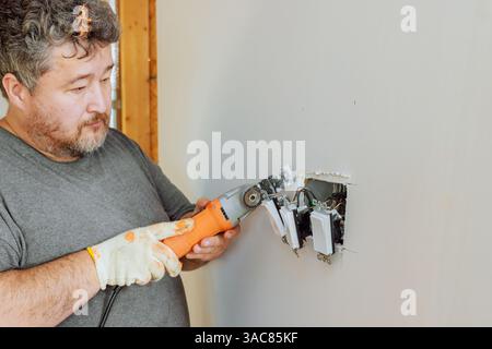 Electrician is using multi tool to work on electrical wiring in wall during home renovation Stock Photo