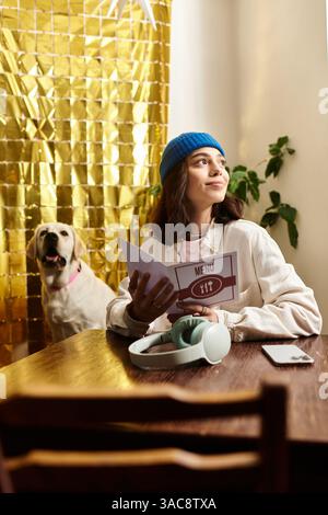 Young woman enjoys her time in a stylish cafe, reading the menu with her labrador by her side. Stock Photo