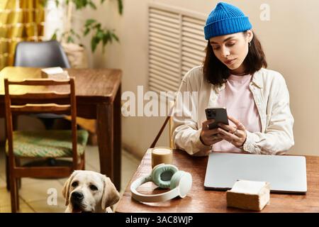 A young woman relaxes in a cozy cafe, focused on her phone while her labrador rests close by. Stock Photo