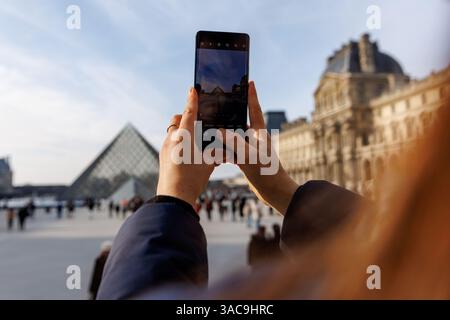 A woman is capturing a photo of the iconic Eiffel Tower using her cell phone Stock Photo