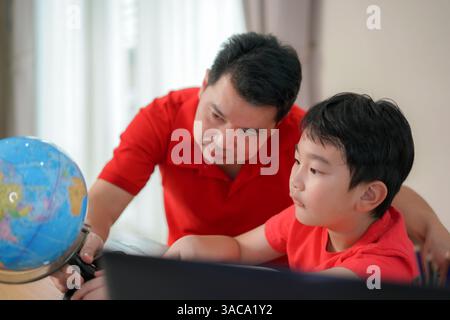 father and son explore the globe at home, nurturing curiosity, bonding, and interactive learning in a cozy family setting. Stock Photo