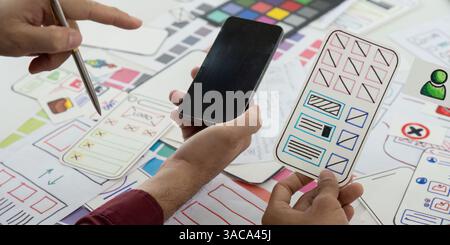 UX Design and Collaboration. Team members reviewing mobile app wireframes on a creative workspace. Stock Photo