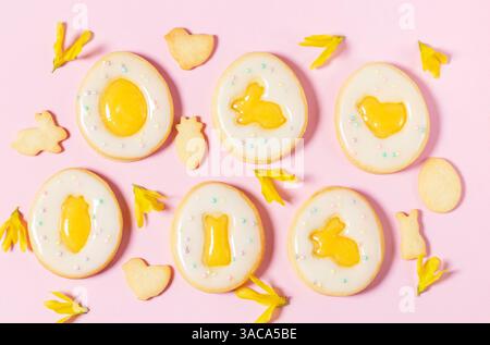 Easter egg cookies with lemon orange curd, covered with white icing and forsythia flowers on a pink background. Selective focus. Stock Photo