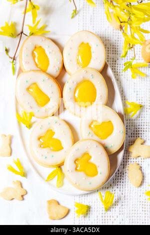 Easter egg cookies with lemon orange curd, covered with white icing and forsythia flowers on a white background. Rustic style, selective focus. Stock Photo