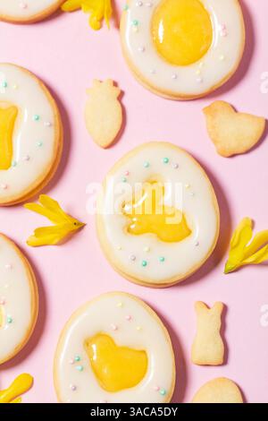 Easter egg cookies with lemon orange curd, covered with white icing and forsythia flowers on a pink background. Selective focus. Stock Photo