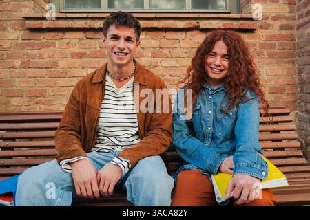 Two joyful students sitting together on a bench, sharing moments of friendship and laughter while discussing their schoolwork and sharing ideas. They are clearly enjoying each other's company and time together Stock Photo