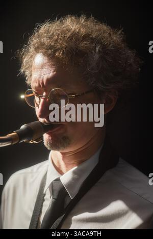Vertical portrait shot of concentrated middle aged male musician playing saxophone with passion performing on stage illuminated by bright spotlight against black background Stock Photo