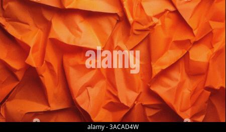 Crumpled orange wrapping paper forms abstract textured background Stock Photo