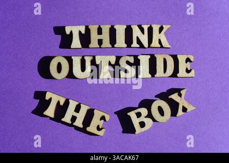 Think Outside The Box, words in wooden alphabet letters isolated on purple background as banner headline Stock Photo