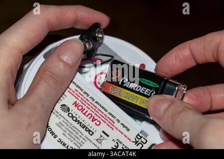 Electrician inserting new battery into the smoke detector Stock Photo