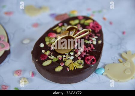 Dubai Chocolate. Luscious dark chocolate, speckled with vibrant freeze-dried raspberry and pistachio, beckons, a golden bunny pendant adding a celebra Stock Photo