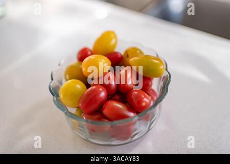 Cherry tomato small vegetable fruit of red yellow color in glass bowl plate, healthy snack macro closeup on white kitchen room table Stock Photo
