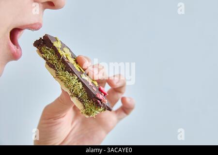 Dubai chocolate. Relish a blissful moment, a single hand reaches for decadent dark chocolate, richly coated in crushed pistachios and juicy raspberry, Stock Photo