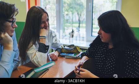 Three high school students collaborate at a desk, discussing and working on a school project together Stock Photo