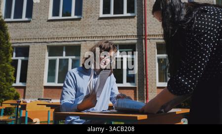 Two high school students working together on a project at an outdoor table near the school building Stock Photo