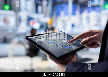 Technician in photovoltaics factory uses tracking software on tablet to review performance of robot arms manufacturing solar panels. Specialist uses device to inspect solar plant machinery, closeup Stock Photo
