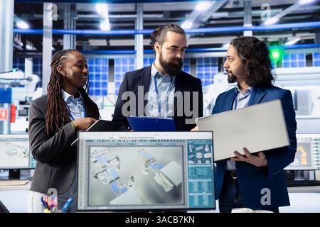 Engineering team in solar panel plant adjusting robotic machinery settings through computer software. Teamworking photovoltaics factory colleagues diagnosing gear performance issues Stock Photo