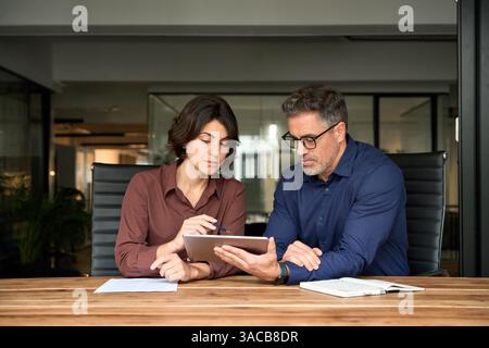 Two busy business colleagues having conversation at office meeting using tab. Stock Photo