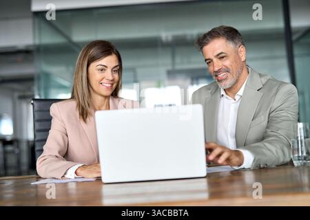 Smiling business woman working on laptop with male colleague at office meeting. Stock Photo