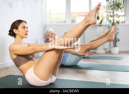 Diligent women practicing upward boat pose of yoga on black mat in fitness room Stock Photo