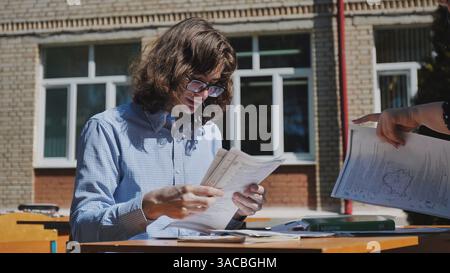 Two high school or university students reviewing their notes and studying together at a table outdoors on a sunny day Stock Photo