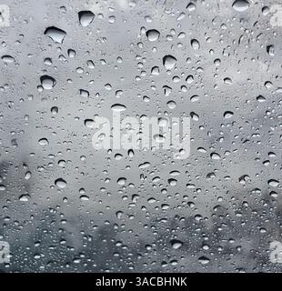 Raindrops accumulate on a windowpane during a cloudy afternoon in the city, creating a serene atmosphere Stock Photo