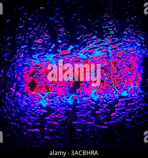 Vibrant neon colors and raindrops create a mesmerizing display on a rain covered window at night Stock Photo