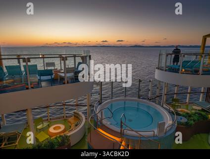 Man watches Roatan sunrise while standing on a deck with chairs and whirlpool Stock Photo