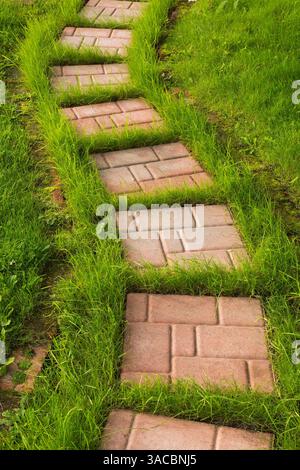 Tan and beige stepping stone path on grass lawn in backyard garden in summer. Stock Photo