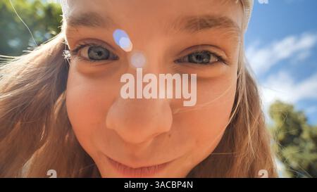 Cheerful schoolgirl pulling silly expressions during bright summer afternoon, laughing outdoors Stock Photo